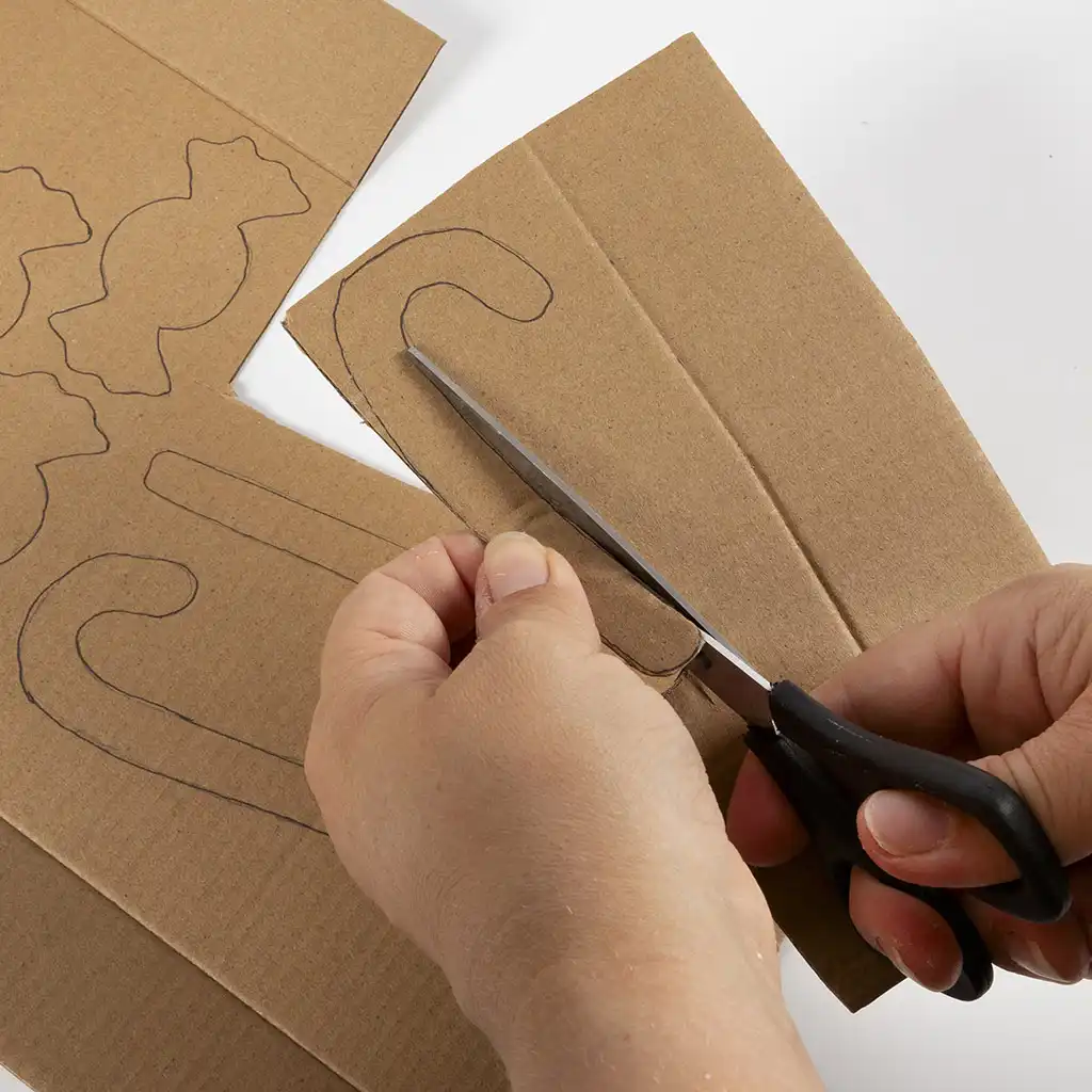 Een schaar knipt de vorm van een zuurstok uit een stuk dik bruin karton waarop ook andere figuren zijn getekend.