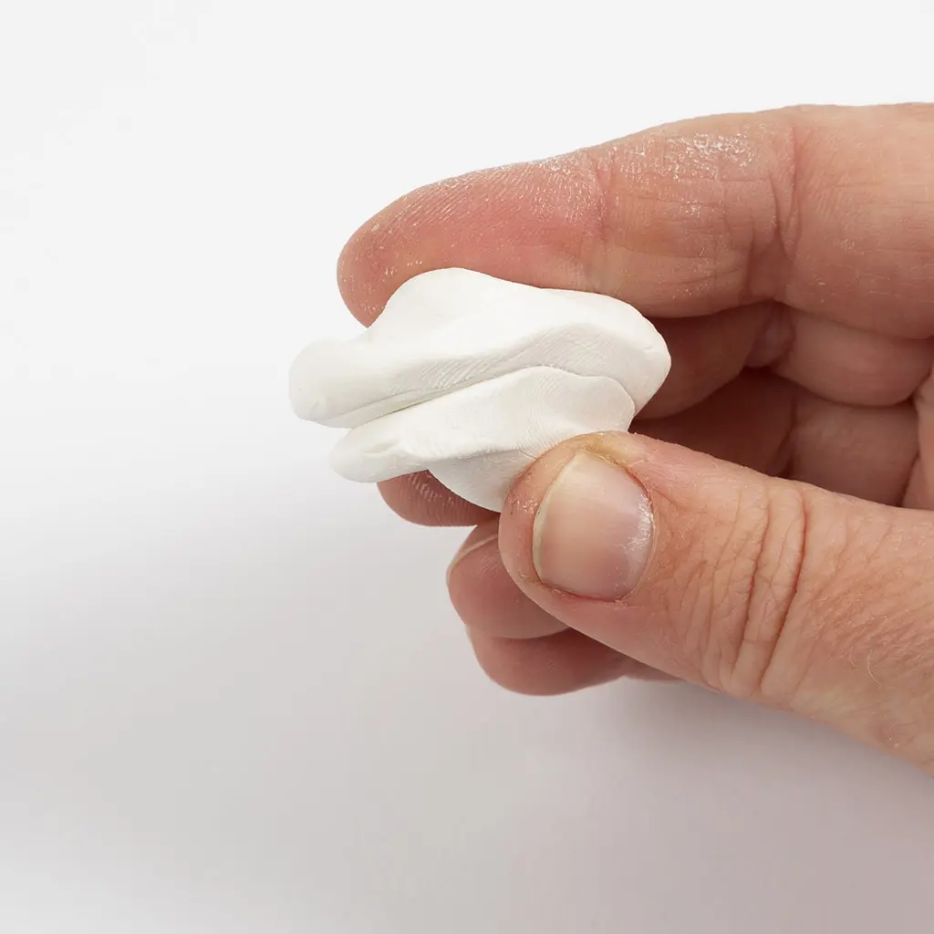 Een hand kneedt een wit stukje klei dubbel om het zacht en soepel te maken.