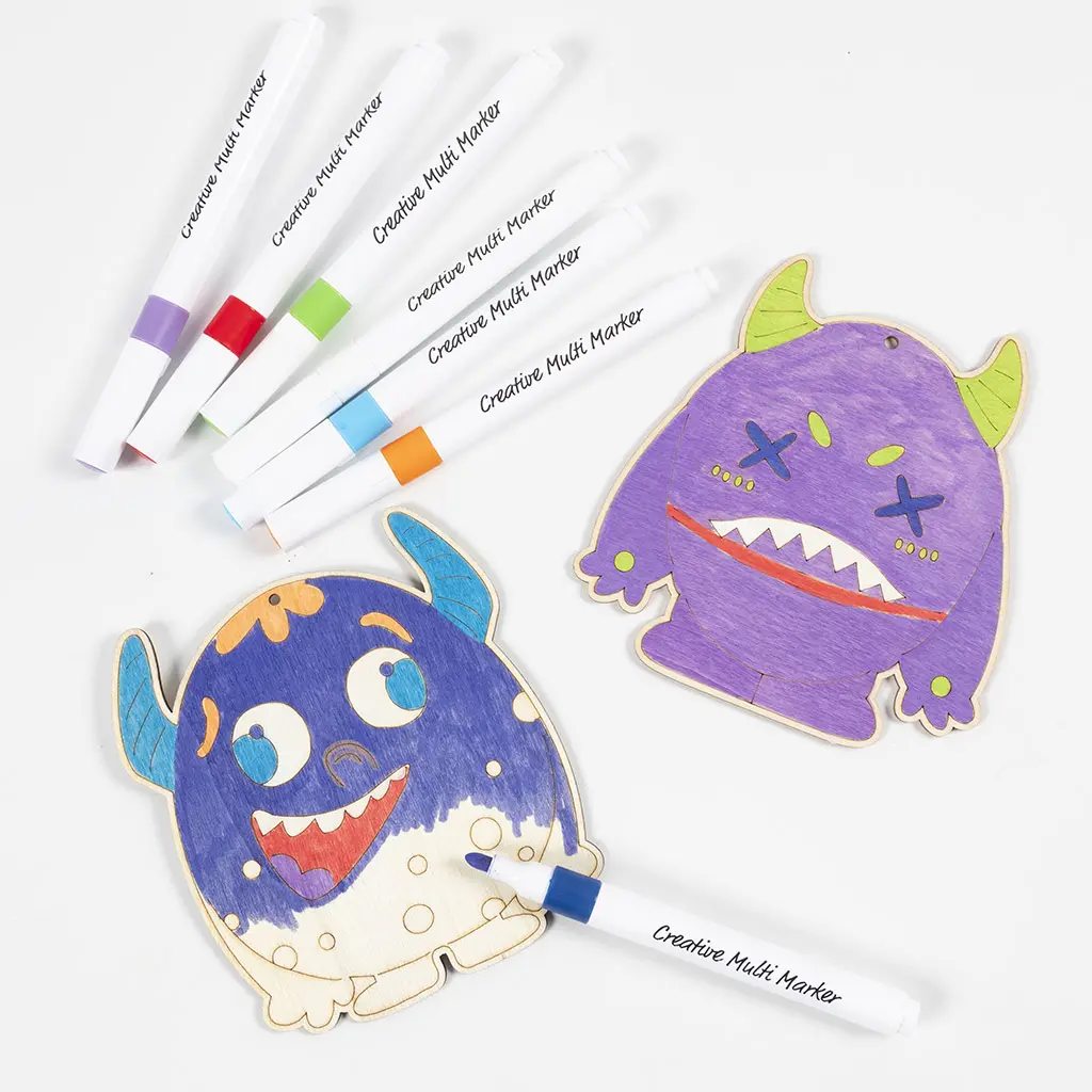 Een bovenaanzicht van twee houten monsterfiguren die worden ingekleurd met viltstiften. Eén monster is paars met groene hoorns, het andere monster wordt ingekleurd met een blauwe stift. Bovenaan liggen zes Creative Multi Markers geordend in een waaier.