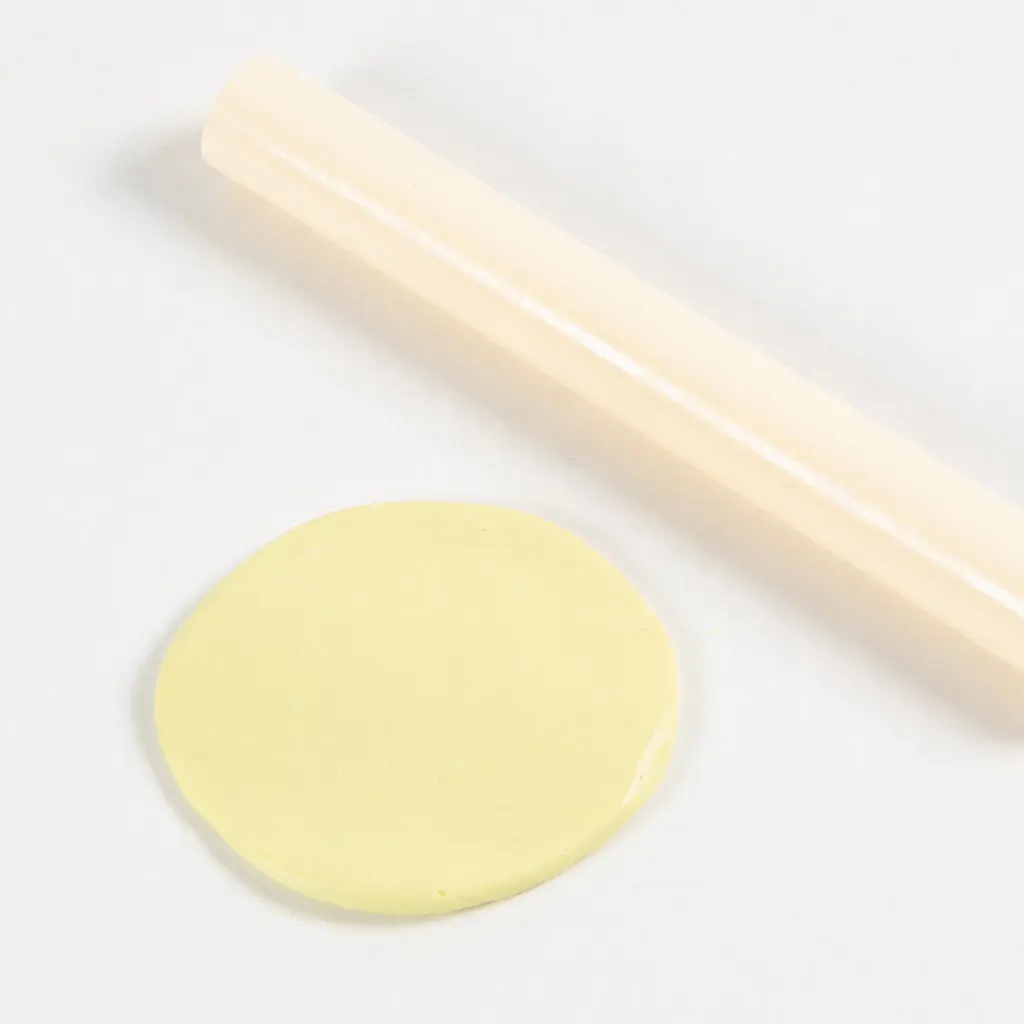Platte gele klei op een witte ondergrond naast een kleine deegroller.