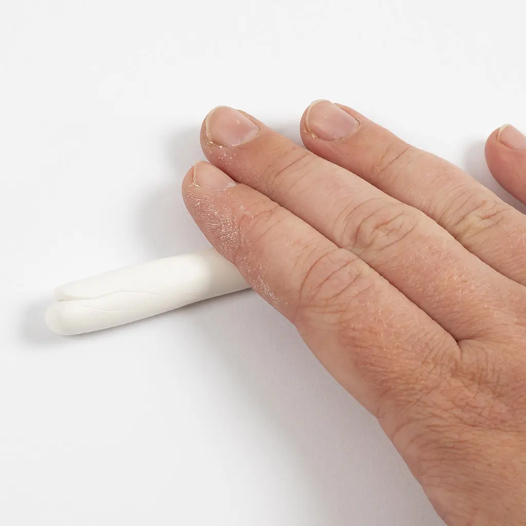 Een hand rolt een stuk witte klei over het werkoppervlak tot een gladde, gelijkmatige string.