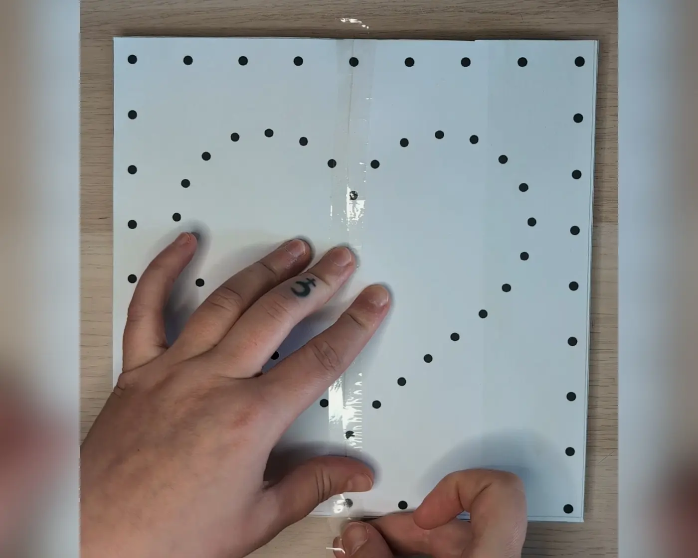 Hand die het papieren patroon met stippen vastzet op een houten plaat
