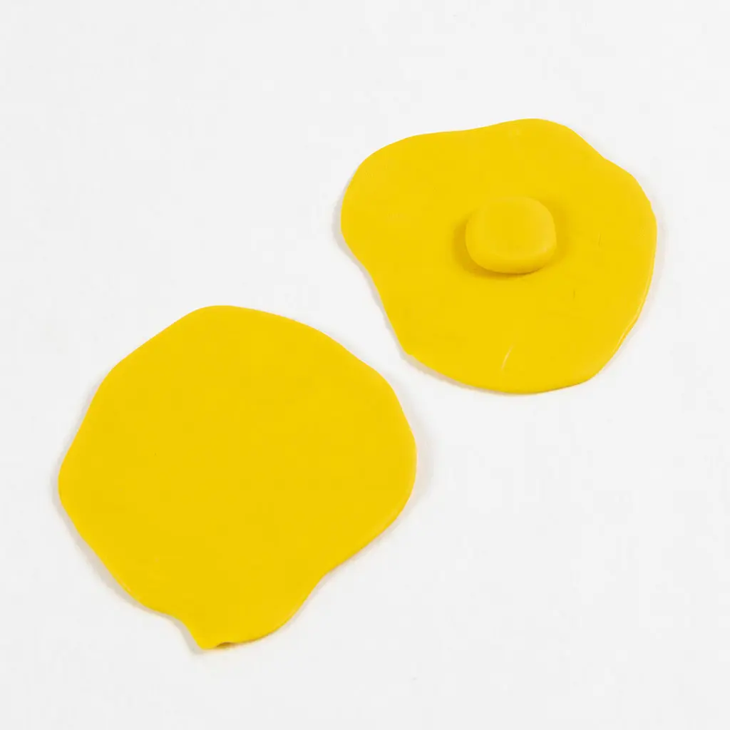 Het kleine, ronde bolletje gele klei is in het midden van de achterste platte cirkel geplaatst, terwijl de andere gele kleicirkel er onveranderd naast ligt.
