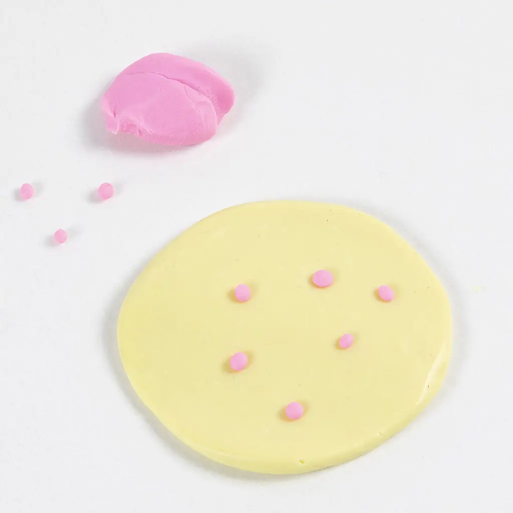 Kleine roze bolletjes klei verdeeld over het ronde vlak gele klei.