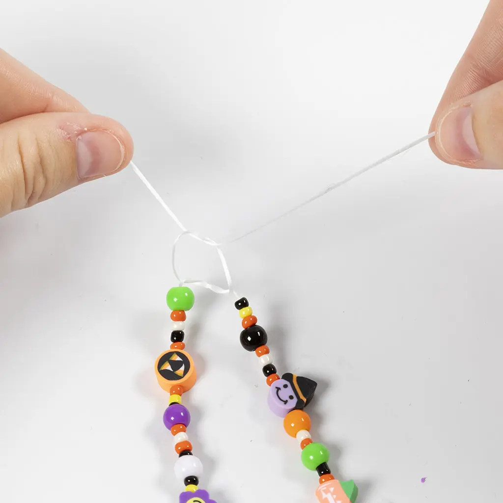 Twee handen die een dubbele knoop strak aantrekken boven de geregen Halloween-kraaltjes.