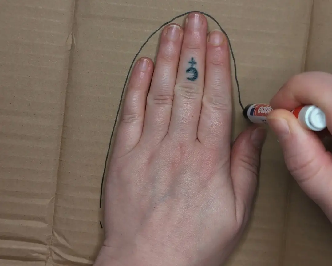hand ligt op karton en wordt overgetrokken met een zwarte stift.