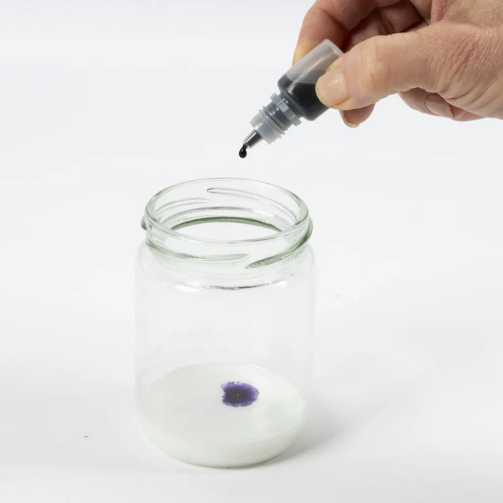 1 glazen pot met gesmolten witte zeep en een druppelaar met paarse kleurstof, 1 druppel in de zeep