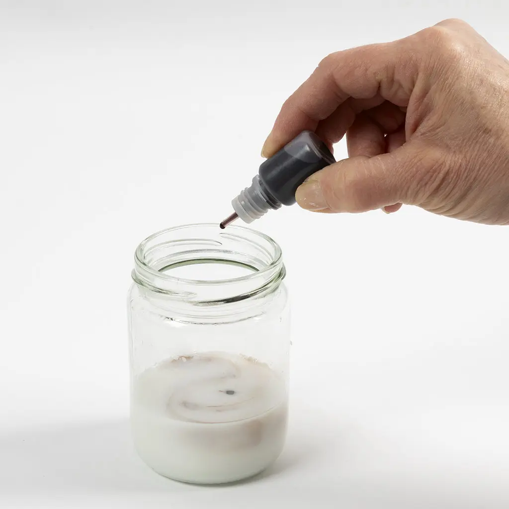 1 glazen pot met gesmolten witte zeep en een druppelaar met brune kleurstof, 1 druppel in de zeep