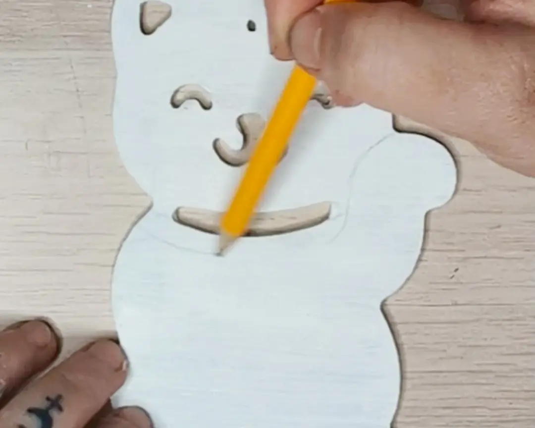 Hand die met een teken potlood details intekent op een wit geschilderde MDF maneki-neko figuur.