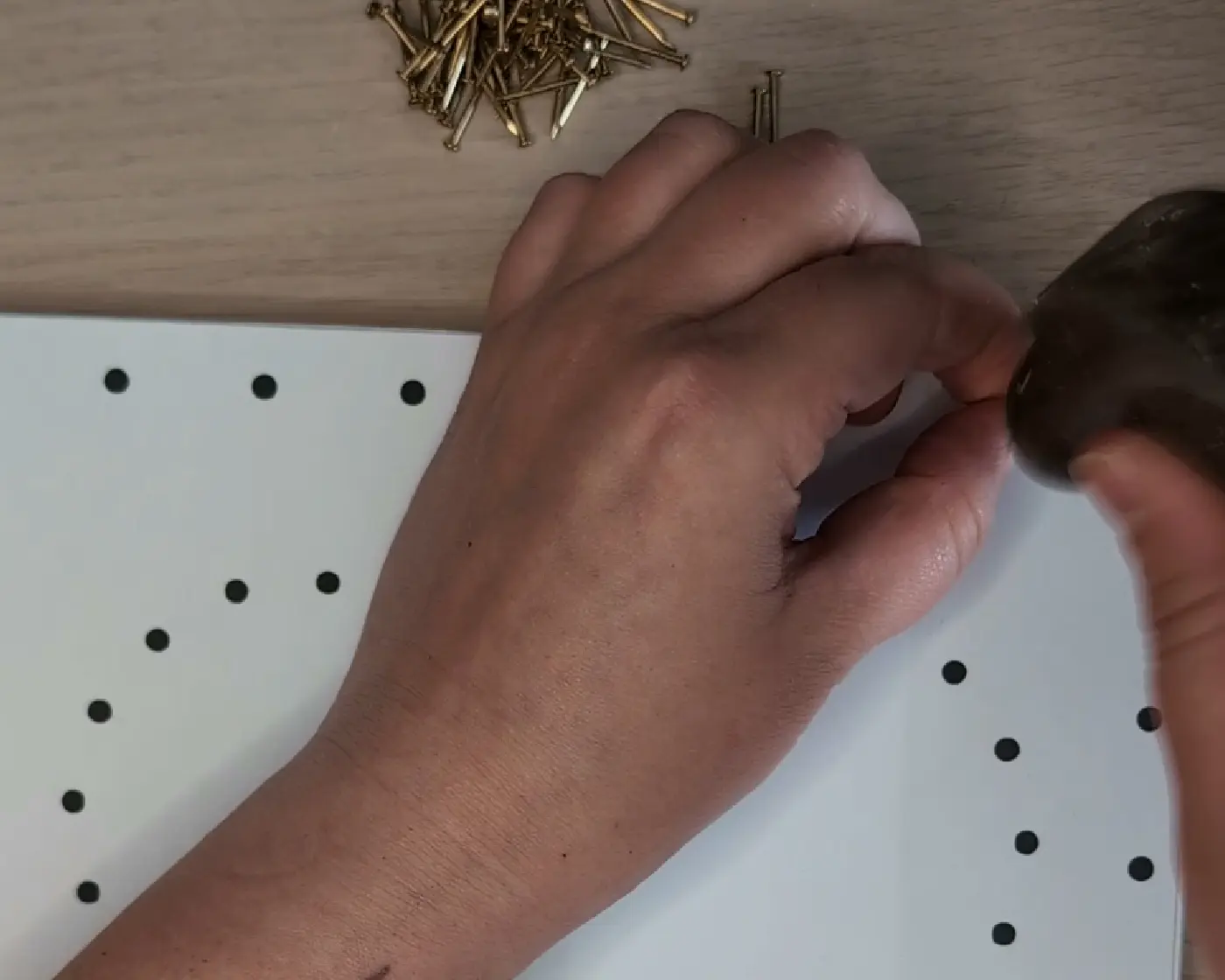 Hand die een gouden spijker inslaat op een stip van het patroon met een hamer, met een stapel spijkers op de achtergrond
