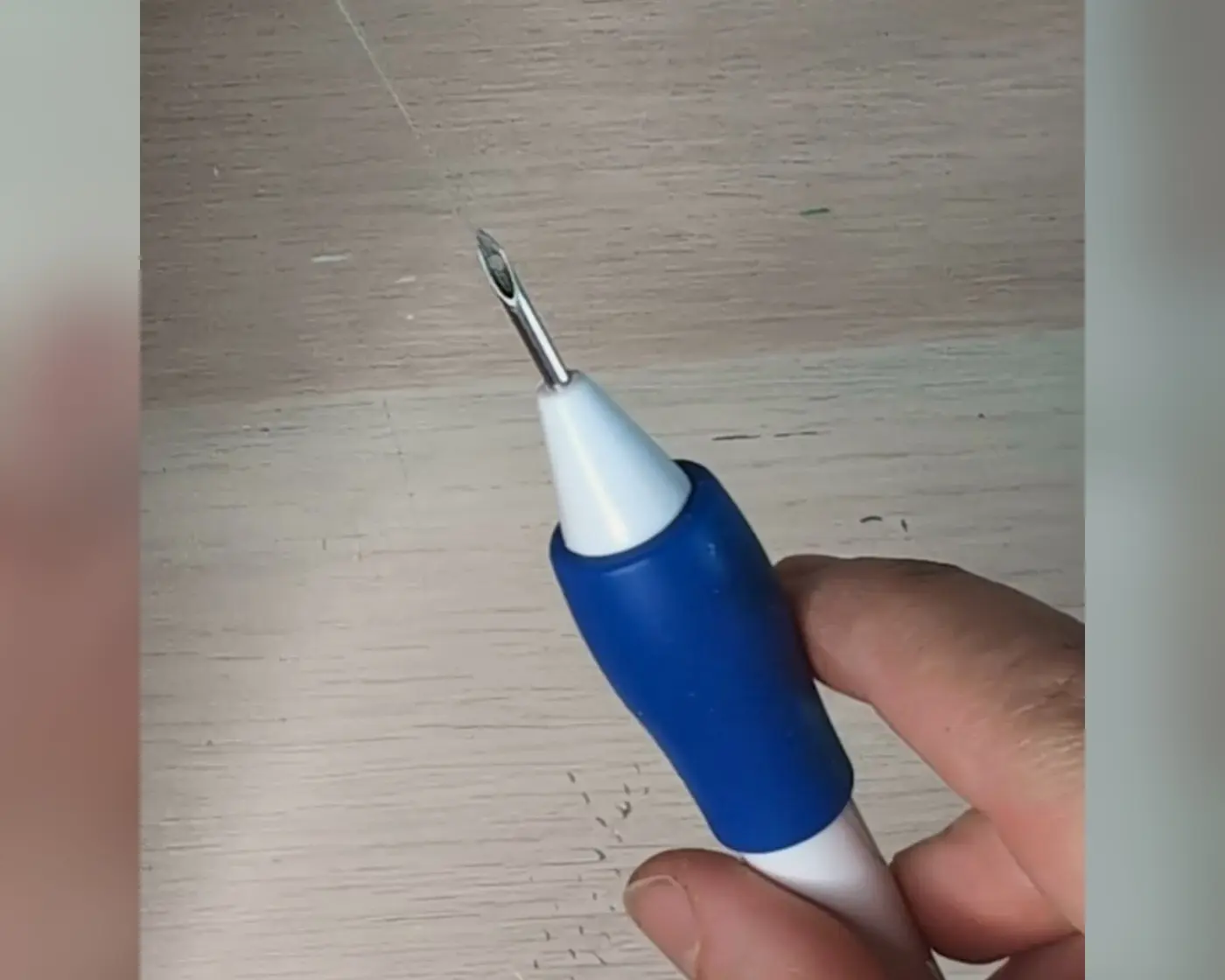 Hand houdt een blauwe punch needle met metalen naald omhoog
