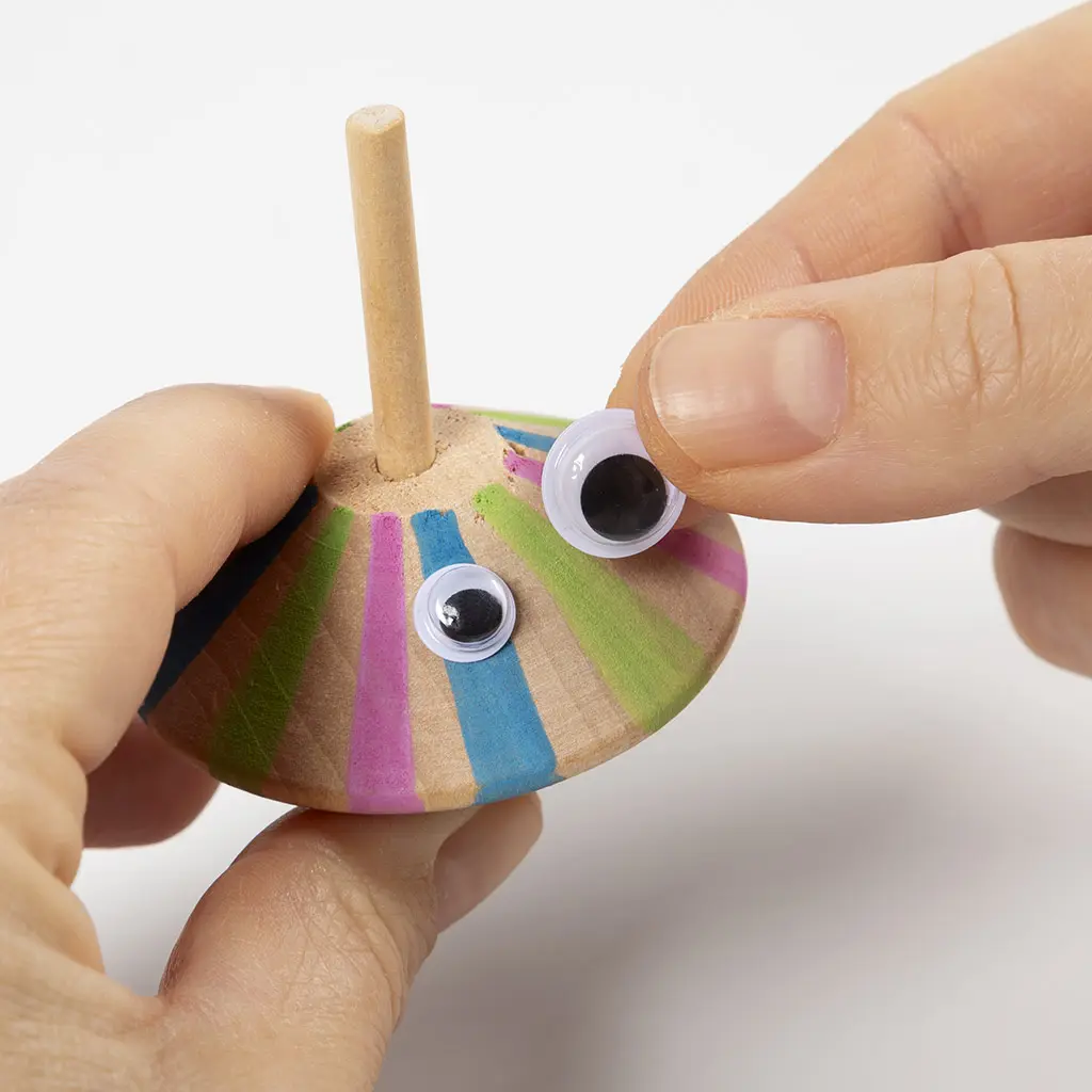 Twee wiebeloogjes worden op het gekleurde vlak van de houten tol geschoven en gekleefd.