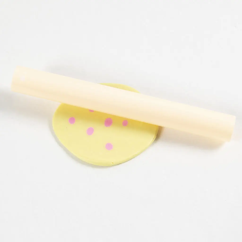 De kleine roze kleibolletjes worden platgewalst in de gele klei met een deegroller.