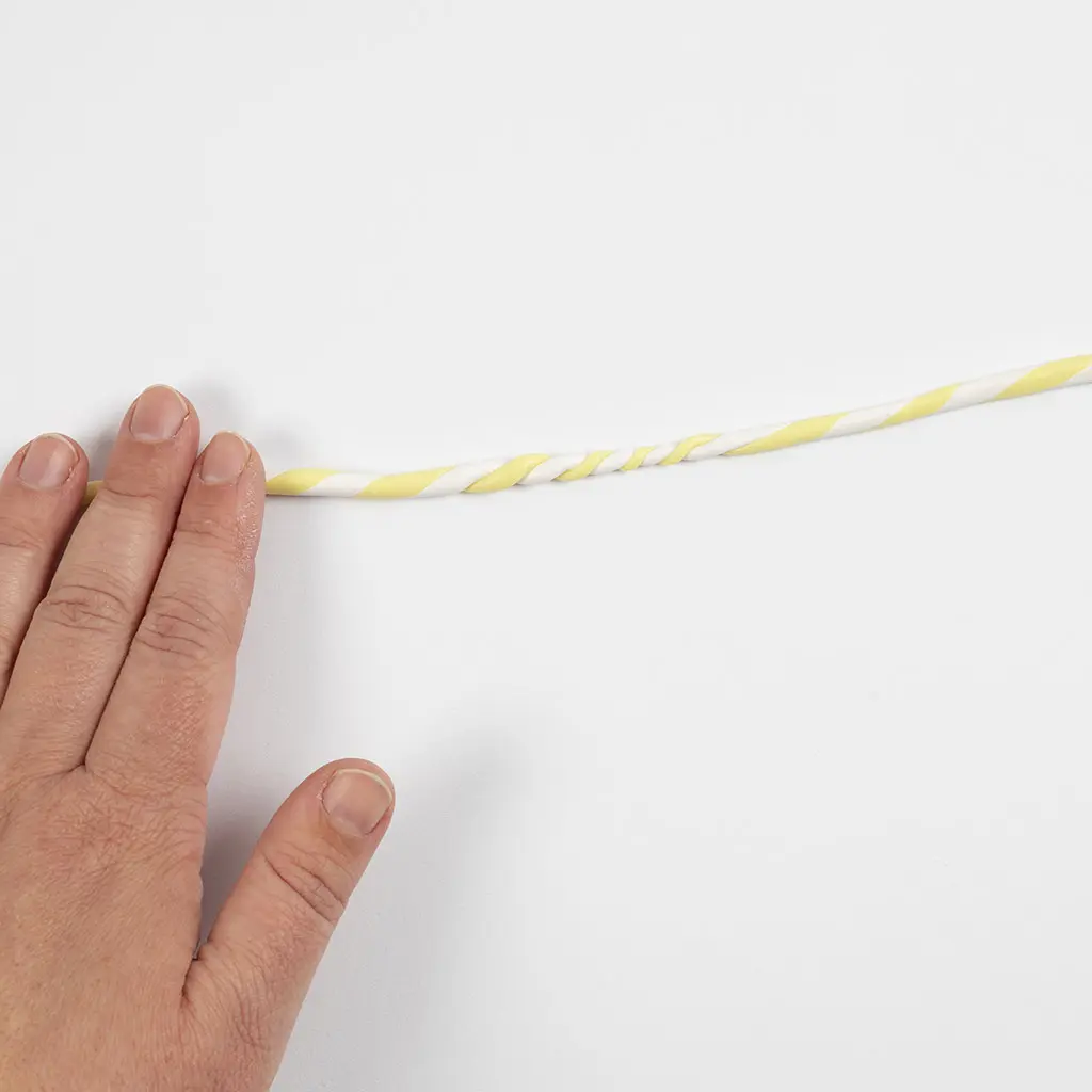 Een hand rolt de in elkaar gedraaide geel-witte kleistring glad over de ondergrond.
