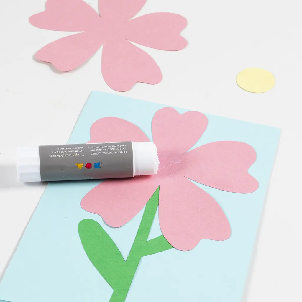 groene bloemensteel is op het blauwe papier gelijmd en daarop het roze papier in de vorm van bloembladeren
