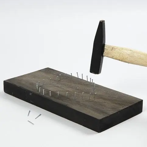 Een hamer slaat kleine spijkers in de houten plank langs de zojuist gemarkeerde vorm van het hart.
