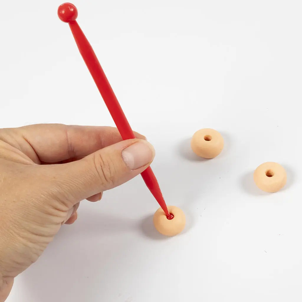 Een rood modelleergereedschap maakt een gat in het midden van een kleibolletje.