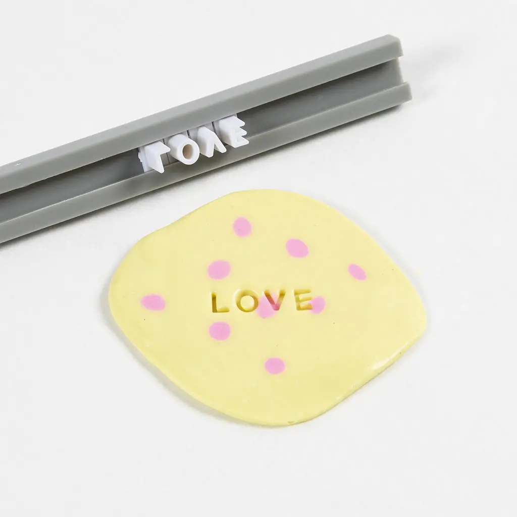 Het woord LOVE wordt met een stempelset in de gele klei gedrukt.