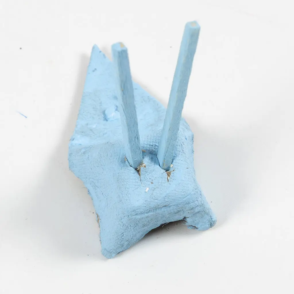 Twee blauwe houten stokjes ingestoken als sprieten in een blauw geverfd stuk eierdooskarton.