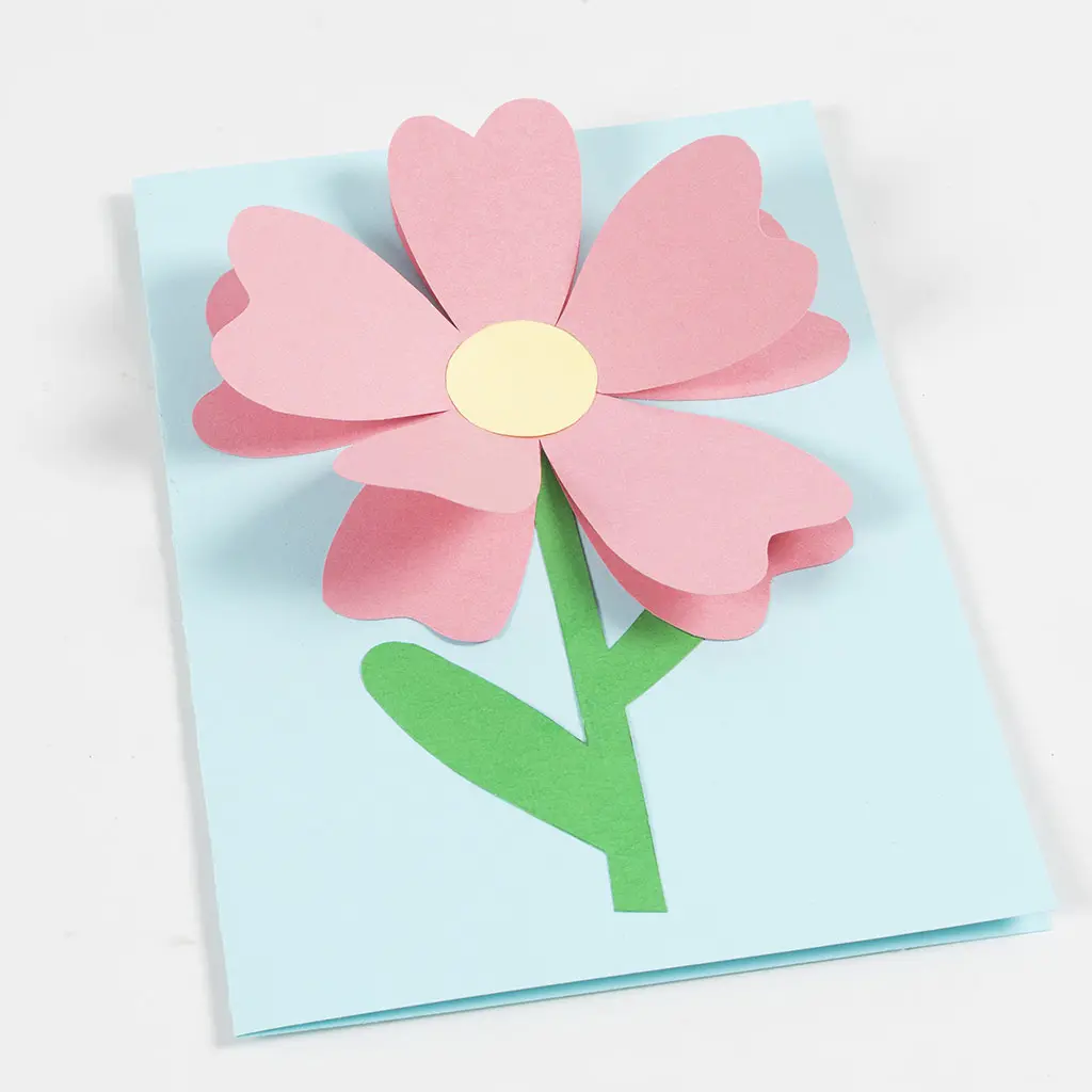 groene bloemensteel is op het blauwe papier gelijmd en daarop het roze papier in de vorm van bloembladeren en daarop een gele cirkel
