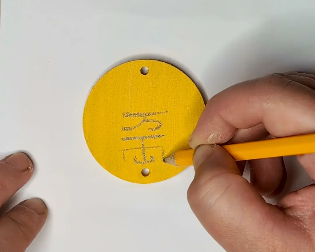 Hand die met een teken potlood Japanse tekens schetst op een geel geschilderde ronde MDF schijf.