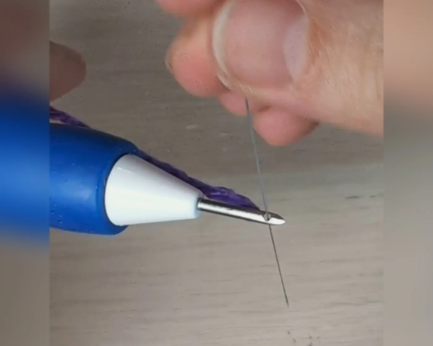 Close-up van handen die paars garen door het oog van de punch needle rijgen