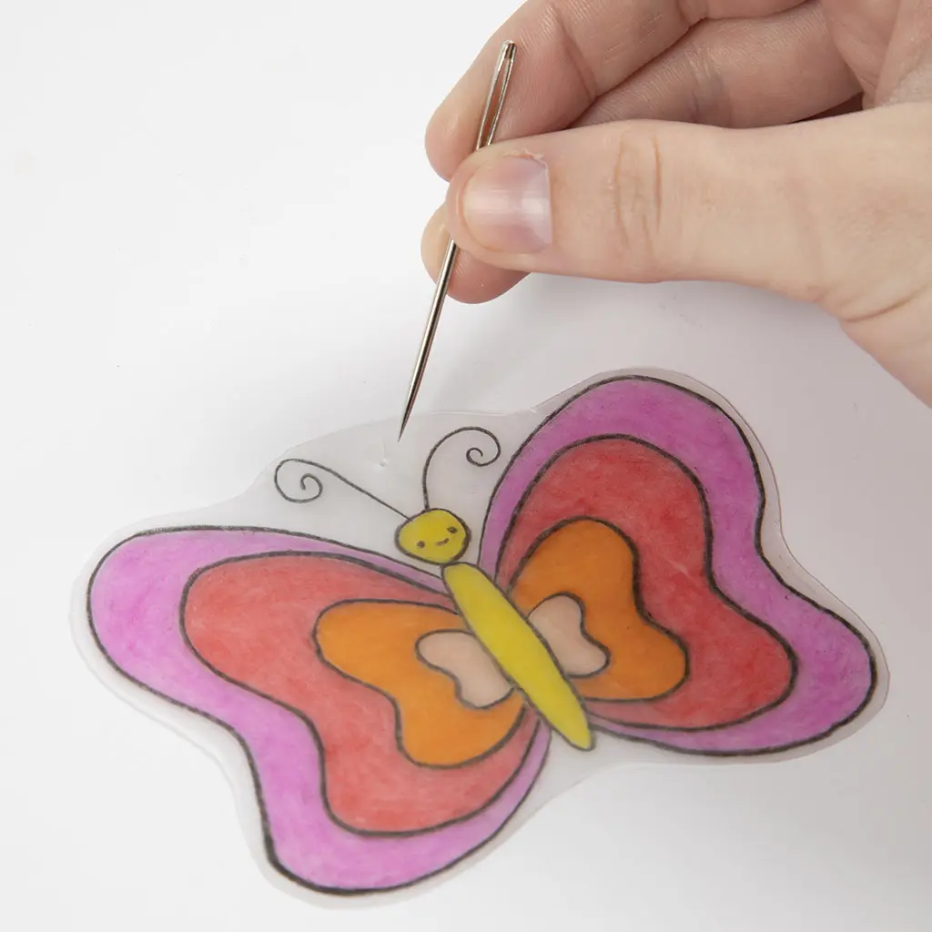 Een hand houdt een metalen naald of prikpen bij een klein gaatje aan de bovenkant van een tweede, rood-roze ingekleurde vlinder.