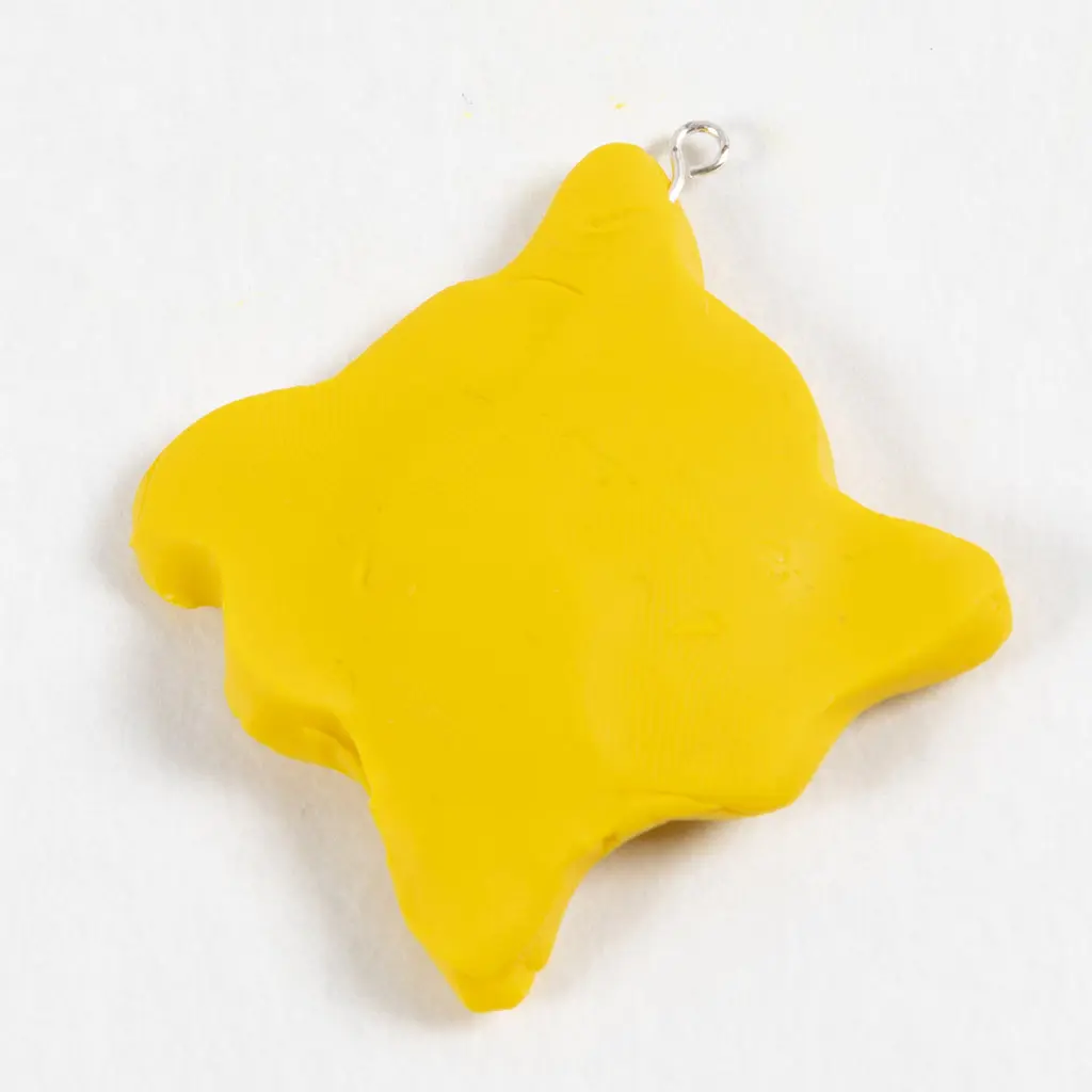 Het uitgesneden gele kleifiguurtje in de vorm van een zon of wolk, voorzien van een klein metalen oogje (oogpen) aan de bovenkant om er later een hanger van te maken.