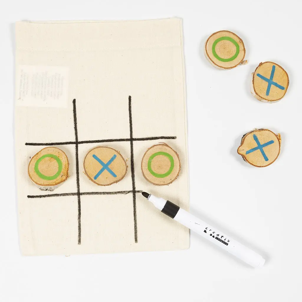 Het stoffen speelzakje is nu voorzien van een volledig raster van twee horizontale en twee verticale zwarte lijnen. Er liggen drie boomschijfjes op het veld en de overige drie liggen ernaast, samen met de zwarte Creative marker.