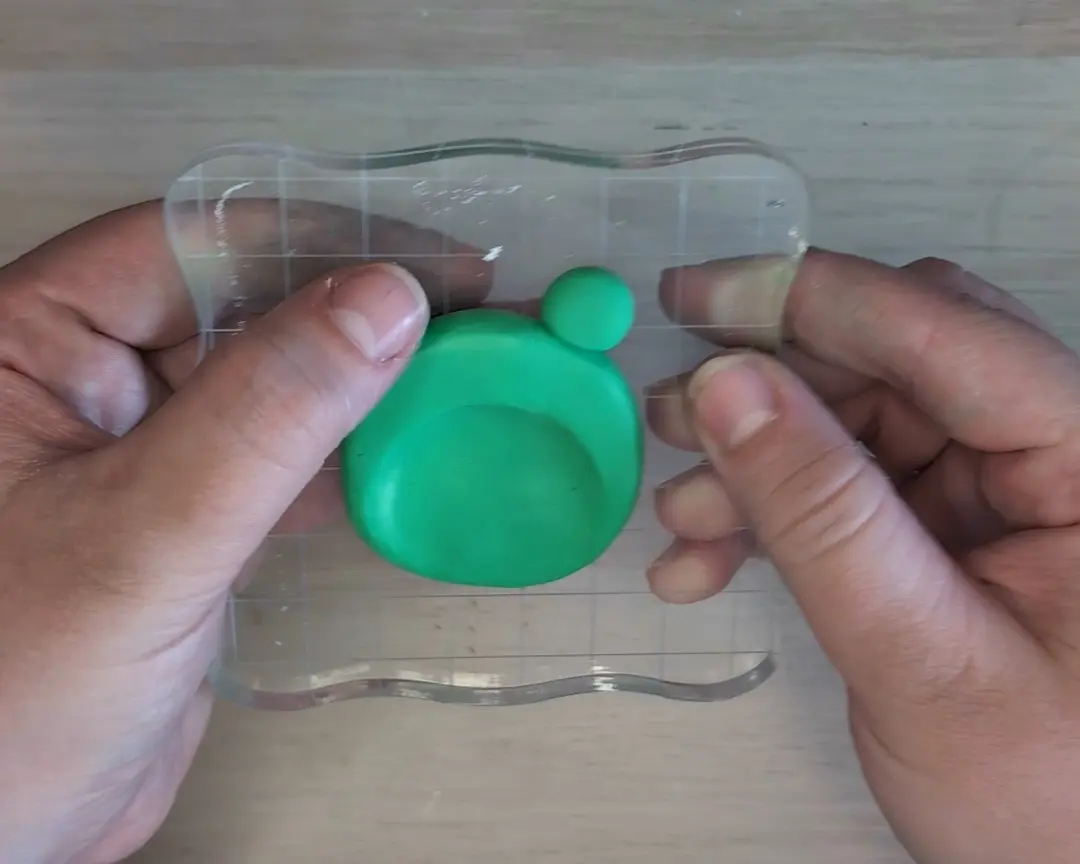 De platte groene schijf met de duimafdruk ligt op het acrylaatblok. Er is één klein groen bolletje aan de bovenkant bevestigd als basis voor het linkeroog.