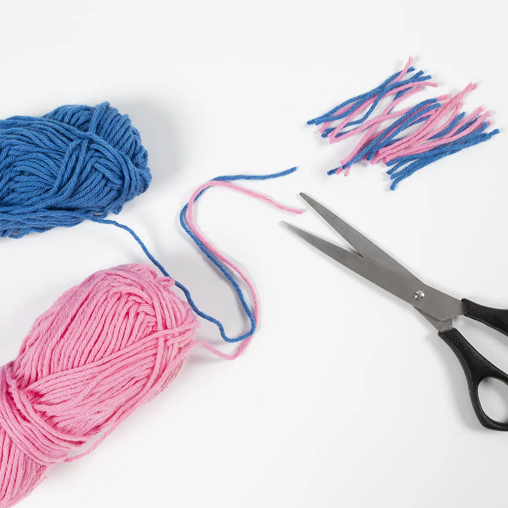 Blauwe en roze bollen wol, een schaar en afgeknipte draadjes wol op een witte achtergrond.