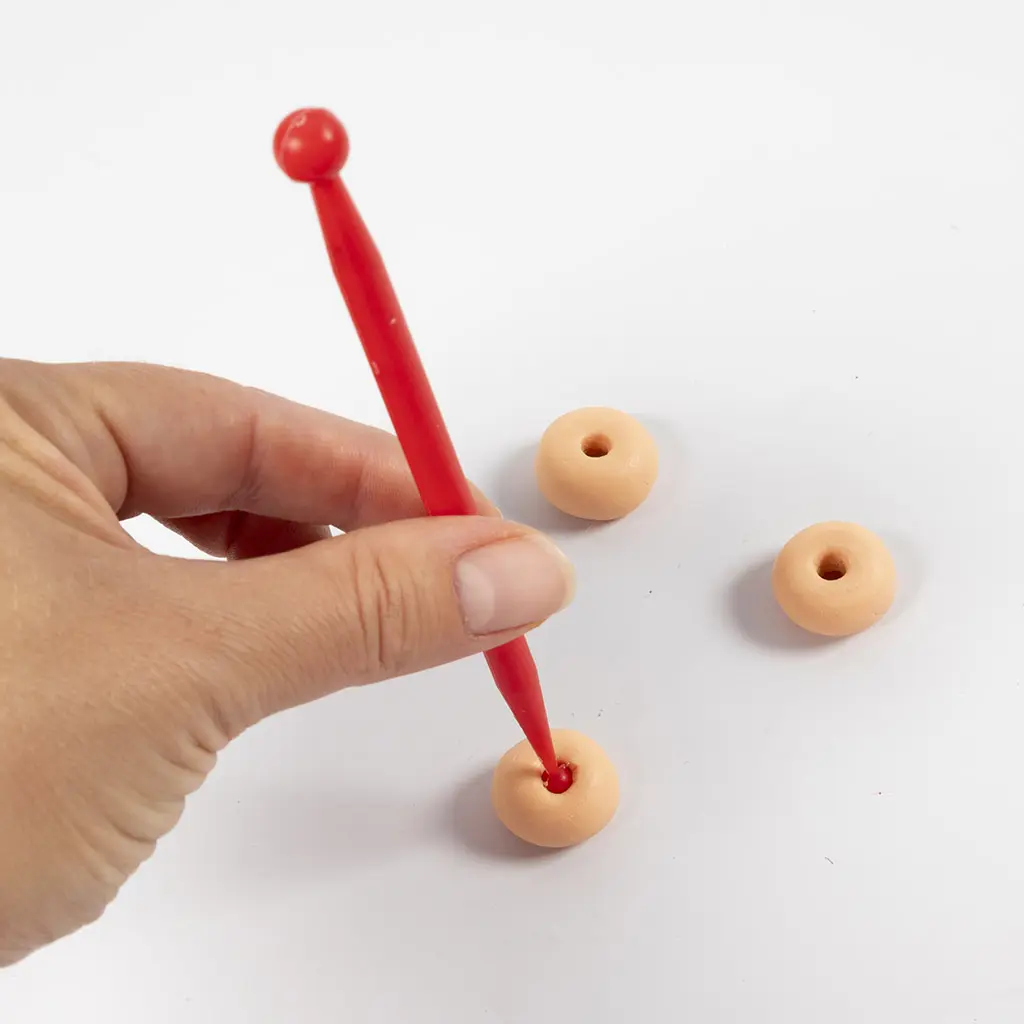 Close-up van het maken van het gaatje in de kleidonut met een rood boetseerpennetje.