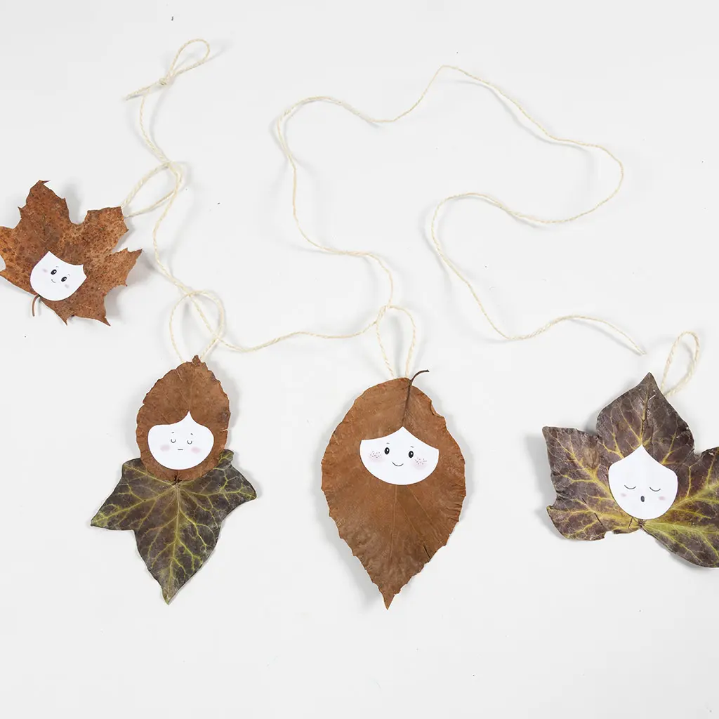 Een opgebouwde herfstling slingers met verschillende bladerfiguren met papieren gezichtjes vastgemaakt aan een jute touw.