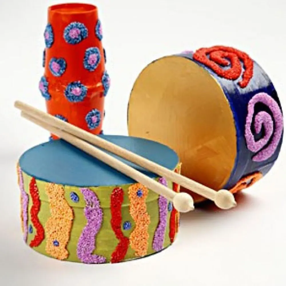 Drie kleurrijk beschilderde, zelfgemaakte muziekinstrumenten (trommels en een schudbeker) gedecoreerd met structurele patronen en klei, met twee houten drumstokjes op de voorste trommel.