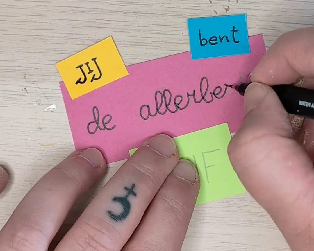 Een hand schrijft met een zwarte marker in sierlijk handschrift 