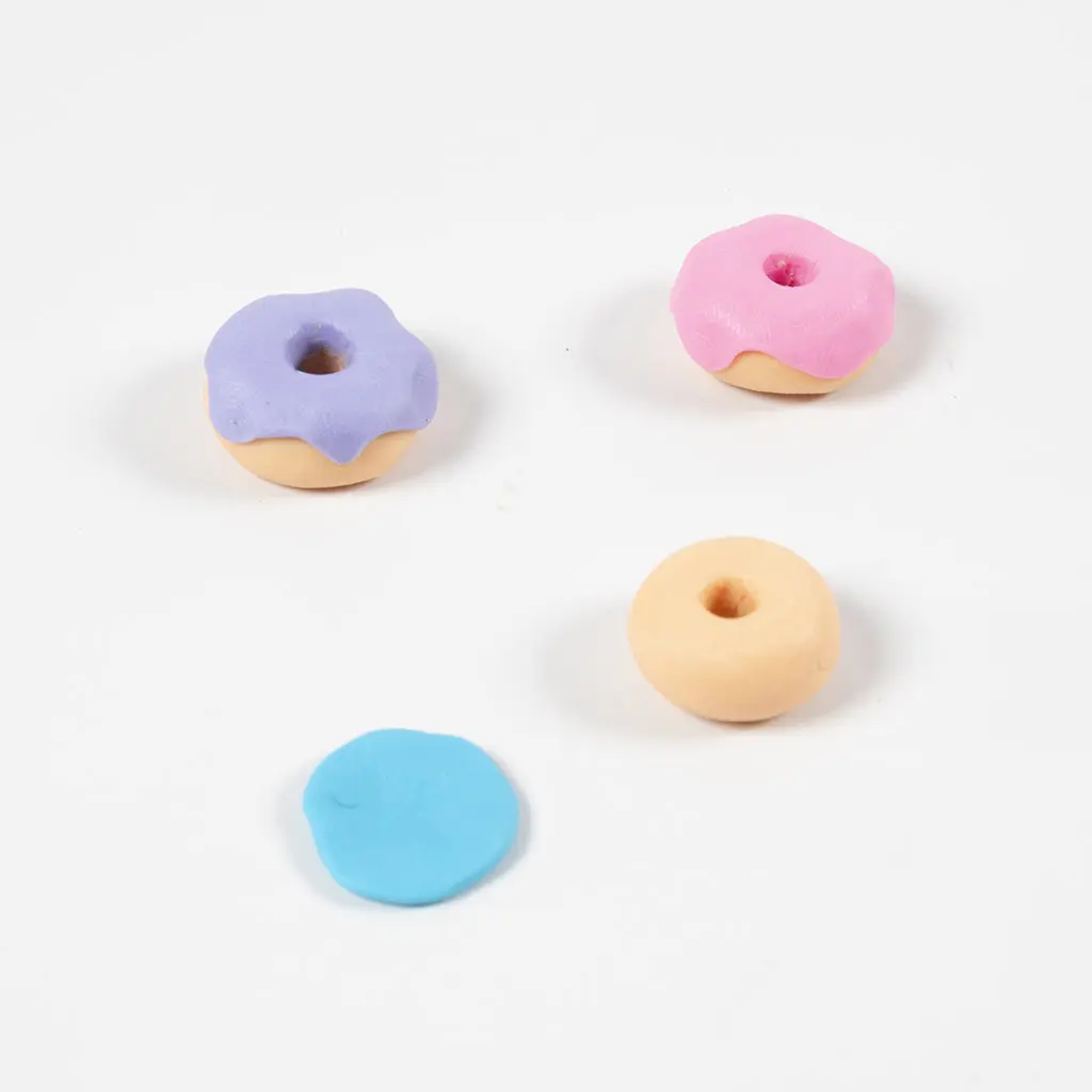 Geelbruine kleidonuts met glazuurlaagjes in paars, roze en blauw uitgespreid op tafel.