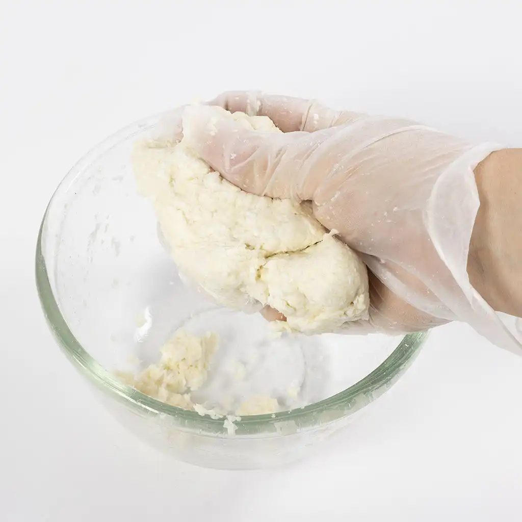 Handschoenen kneden een stevige mengeling van papierpulp en water tot een natte massa in een glazen kom.