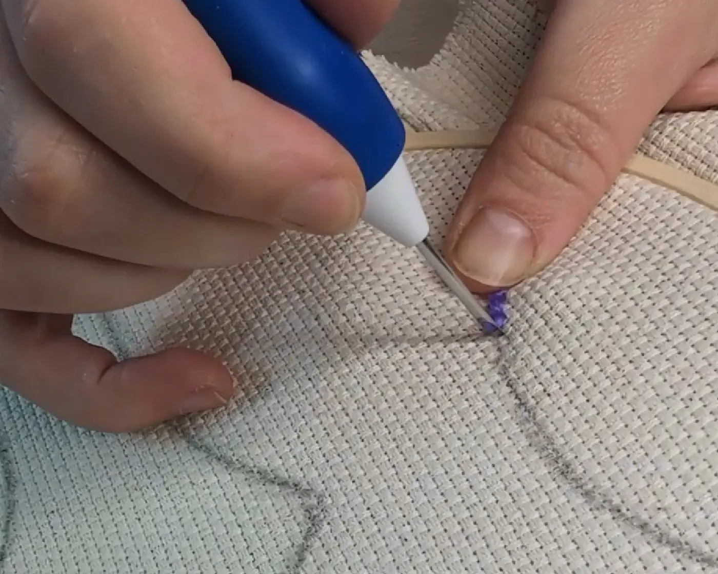 Hand die de punch needle in de stof steekt om de eerste steek te zetten langs het potloodontwerp