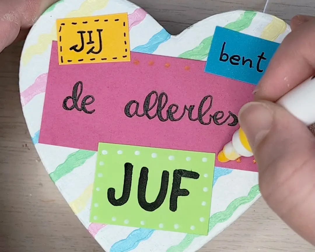 Een hand lijmt met een witte lijmstift kleurrijke kaartjes met de tekst 