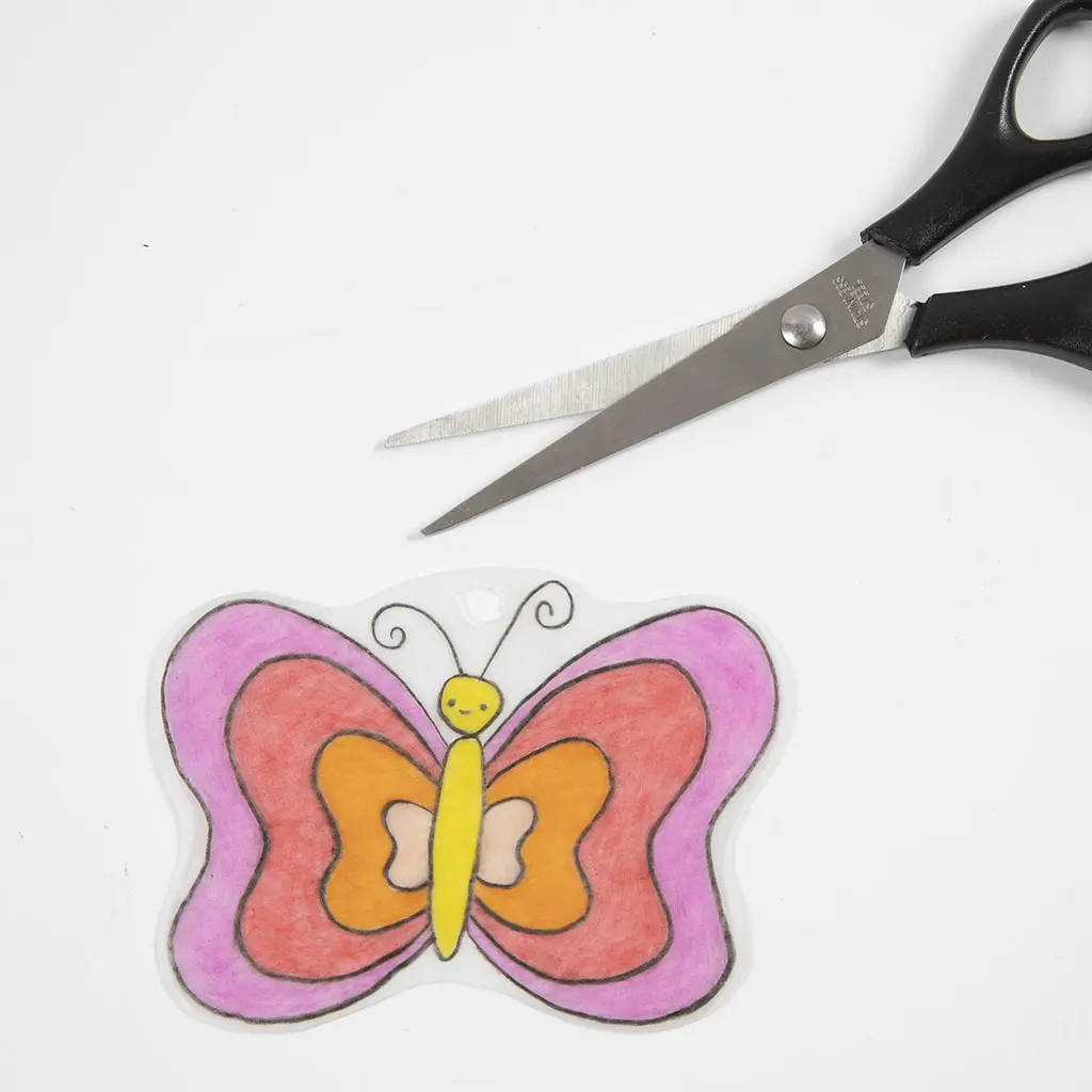 De netjes uitgeknipte rood-roze vlinder ligt klaar op een witte ondergrond met de schaar er vlak boven.