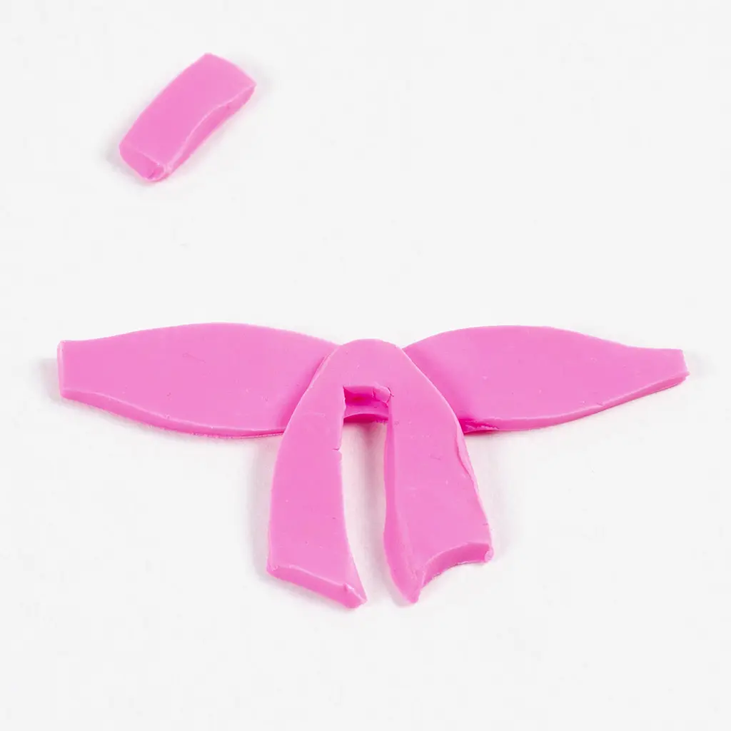 De eerste stappen voor het samenstellen van de roze kleistrik. De twee neerhangende linten (gemaakt van klei) zijn in het midden op de vlakke basisstrook geplaatst.