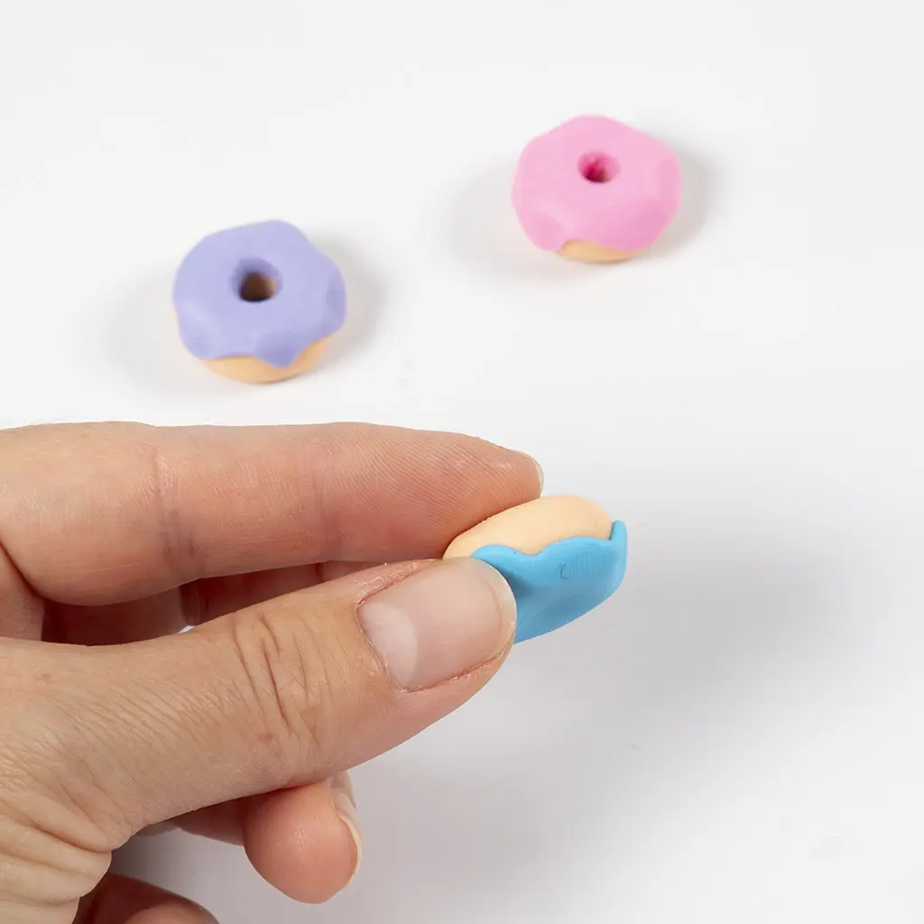 Het blauwe glazuurlaagje van klei wordt voorzichtig op de basis van de donut gedrukt.