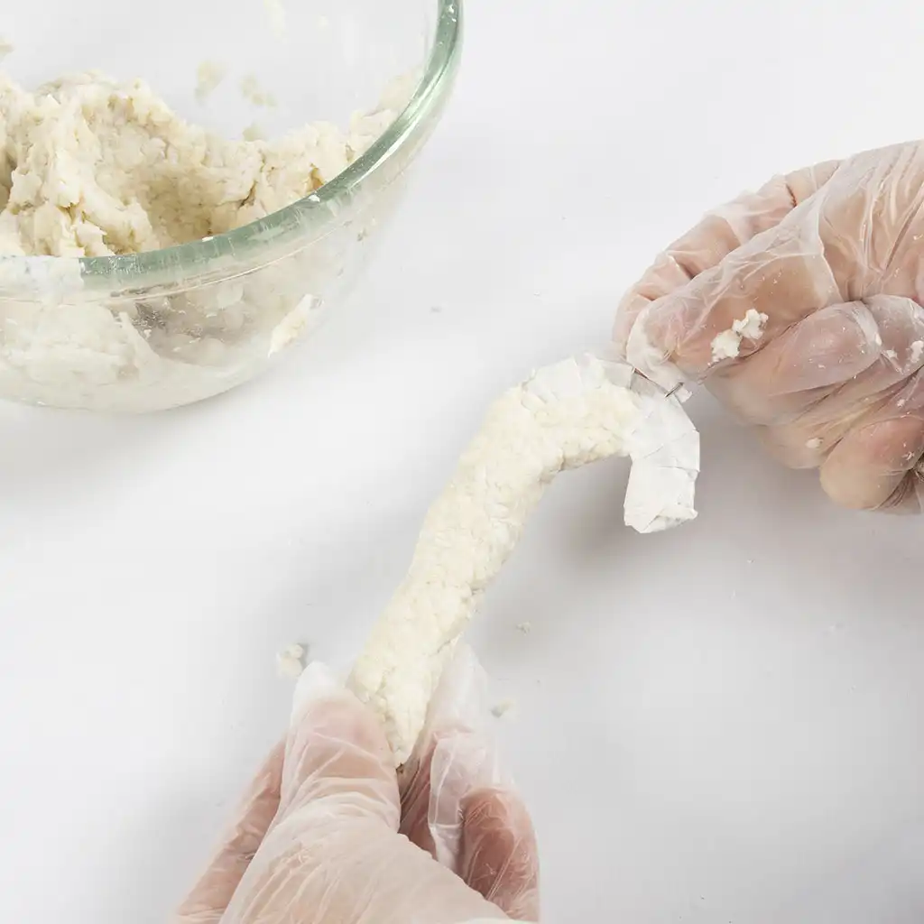 Met de hand wordt een dunne laag natte papierpulp rondom de omwikkelde kartonnen zuurstok aangebracht.