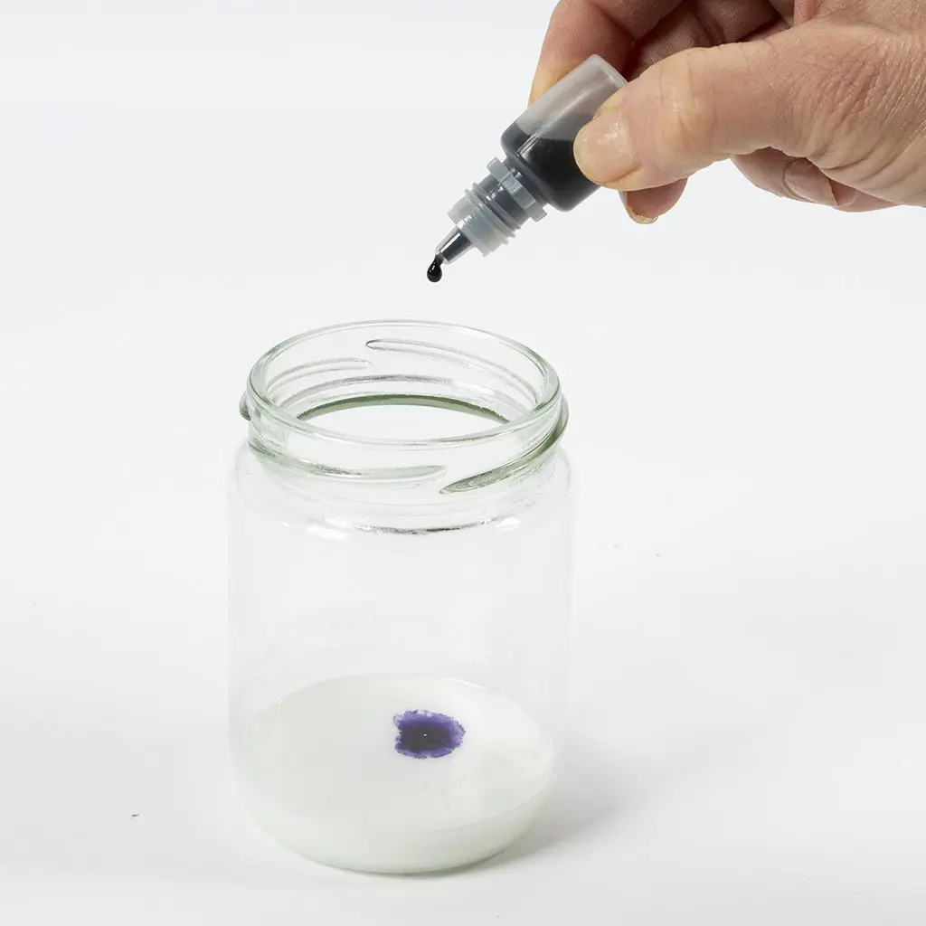 1 glazen pot met gesmolten witte zeep en een druppelaar met paarse kleurstof, 1 druppel in de zeep