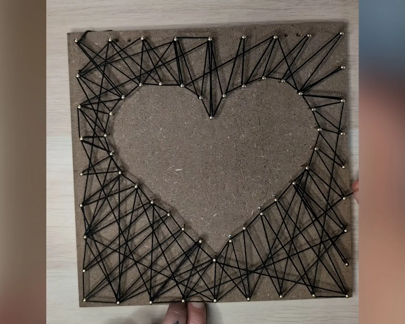 Afgewerkt string art bord met een hartvorm omgeven door een geometrisch patroon van zwart garen gespannen tussen gouden spijkers