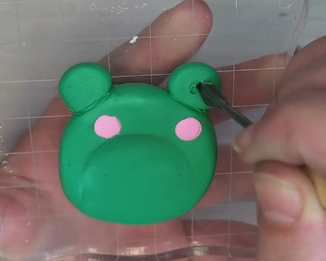 Een hand gebruikt een fijne metalen spatel om uitsparingen in de oogkas van de kikker te maken.
