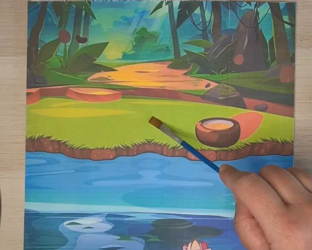 Hand houdt een penseel boven een geïllustreerde achtergrondprint van een tropisch junglelandschap met een rivier en waterlelies.