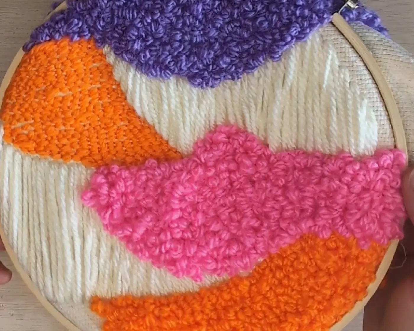 Punch needle werkstuk in een houten borduurring met kleurrijke abstracte golvende vlakken in paars, oranje en roze garen