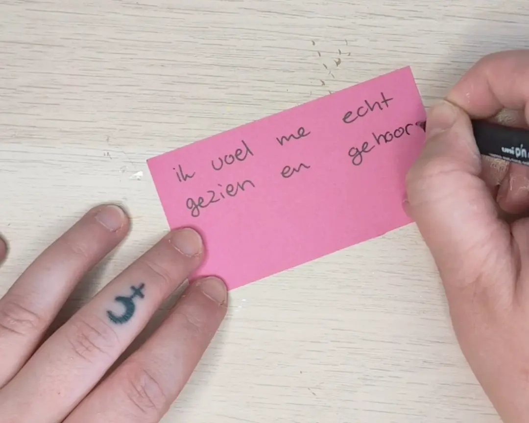 Een hand schrijft met een zwarte uni PIN marker de tekst 