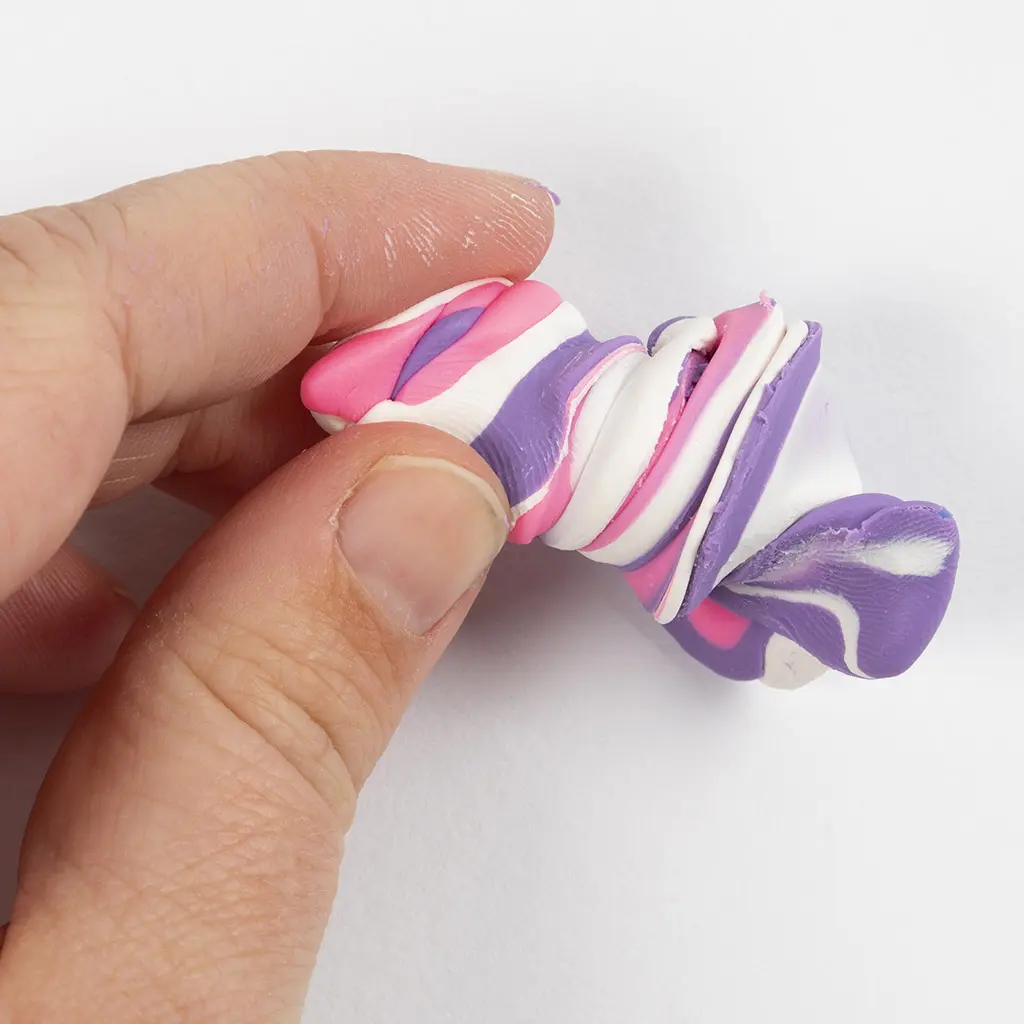 Een hand tordeert en draait de gevouwen paars, roze en witte klei om een margetextuur of geglazuurd effect te creëren.